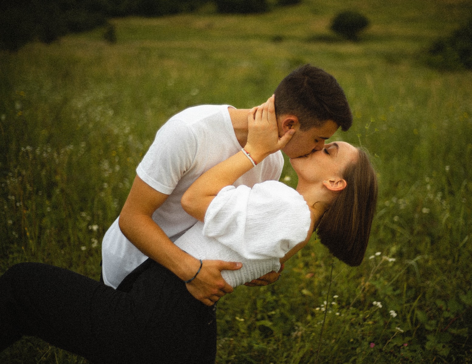 man in white t-shirt kissing woman in white shirt on green grass field during daytime