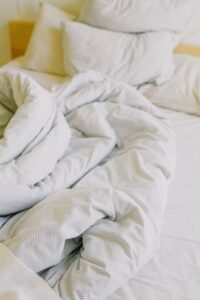 From above of comfortable messy with soft white blanket and pillows in sunny morning